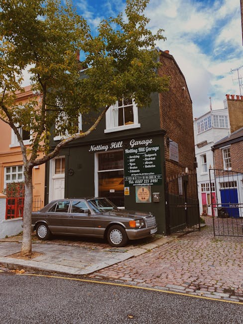 A two-storey building painted dark green with white window frames, labeled as 'Notting Hill Garage' and advertising car sales and repairs, is situated on a street corner. In front of the building, a d